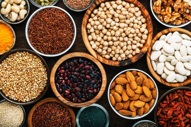 Superfoods, legumes, nuts, seeds and cereals set in bowls on wooden background. Superfood as chia, spirulina, beans, goji berries, quinoa, turmeric, mung bean, buckwheat, lentils, flax seed, wild rice and almond. Copy space, top view